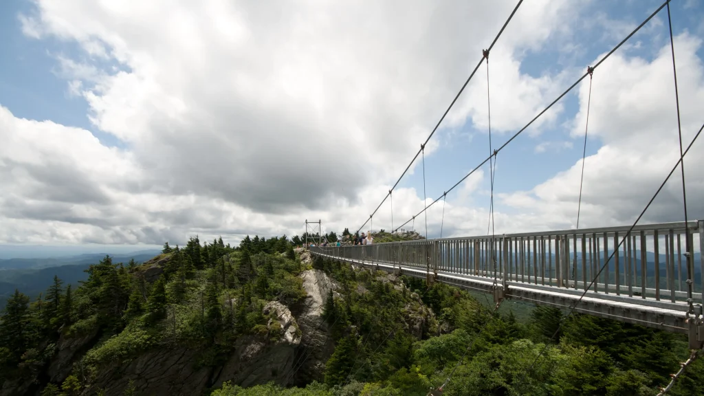 Mile High Swinging Bridge spanning rocky forested peaks beneath large clouds